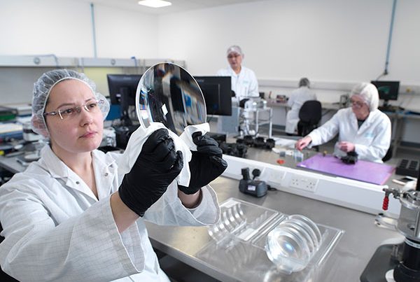 woman in white coat, hairnet and glasses inspecting large diameter lens